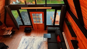 A cozy cabin interior with a large window, wooden walls, a ceiling light fixture, a sofa, and a small table. - Pentalow Cabin (Kartepe)