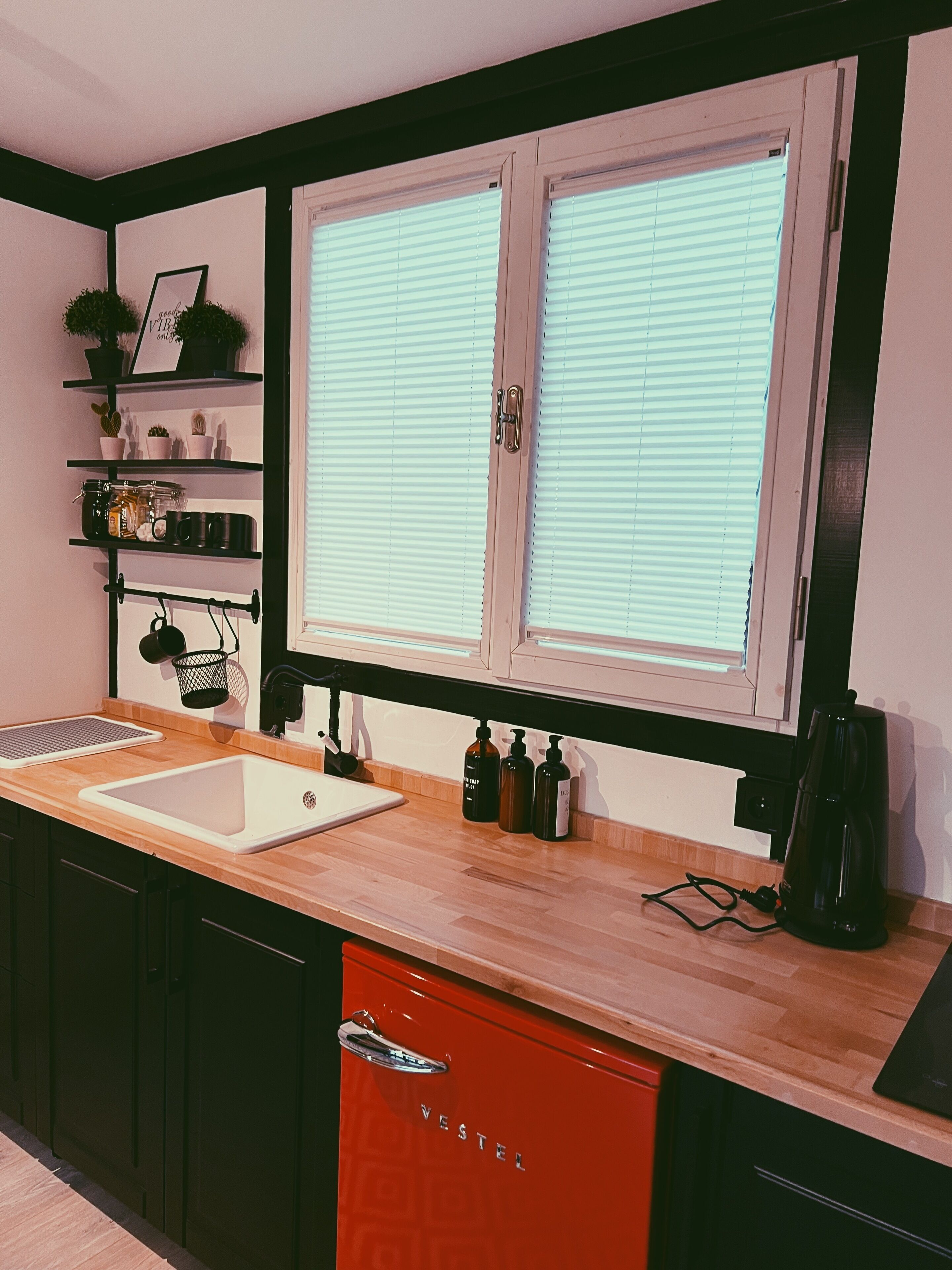 Une cuisine avec un évier blanc, un plan de travail en bois, des placards noirs et un lave-vaisselle rouge.