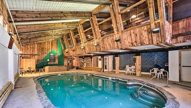 Una piscina interna con travi in legno, uno scivolo verde e sedie a sdraio.
