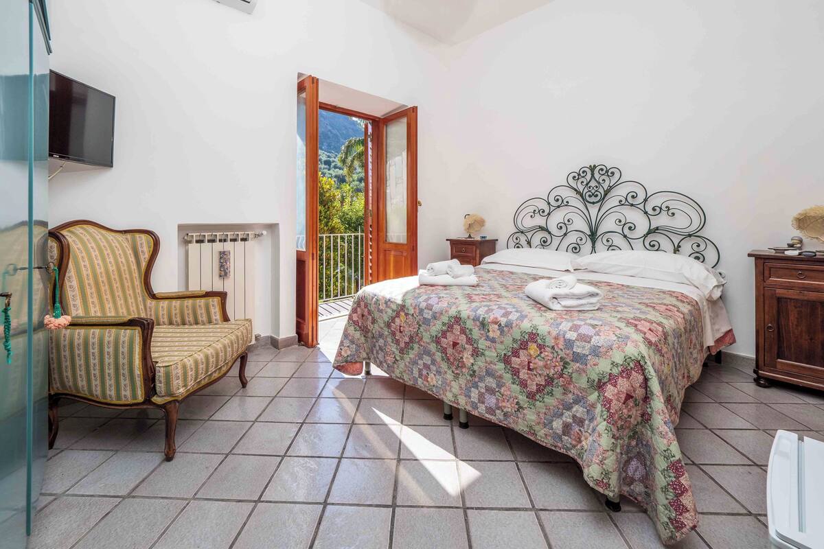 Un dormitorio con cama, una silla, un televisor, un radiador y un balcón con vistas a las montañas.