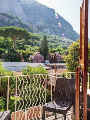 A balcony with a wicker chair, a view of a mountainous landscape, and a white fence. - Maison Rosa (Meta)