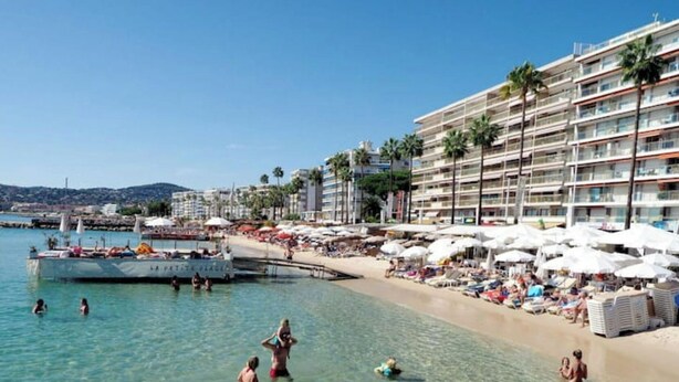 Une plage à l’eau claire, où l’on peut se baigner, et un hôtel doté de nombreux balcons et de parasols.