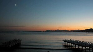 Une vue sur la côte, avec une jetée s’avançant dans des eaux calmes, un ciel dégagé et un croissant de lune.