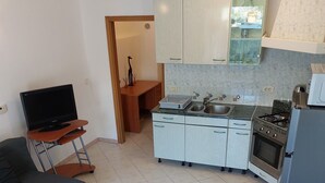 A compact living space with a kitchenette, a sofa, a TV on a stand, and a dining table.