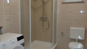 A bathroom with a shower enclosure, a toilet, and a washing machine.