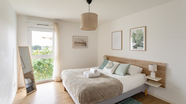 Ein modernes Schlafzimmer mit einem großen Bett, einem stehenden Spiegel, einem Fenster mit Vorhängen und einer Deckenleuchte.