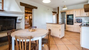 Una cocina con mesa redonda, sillas de madera, chimenea y electrodomésticos modernos.