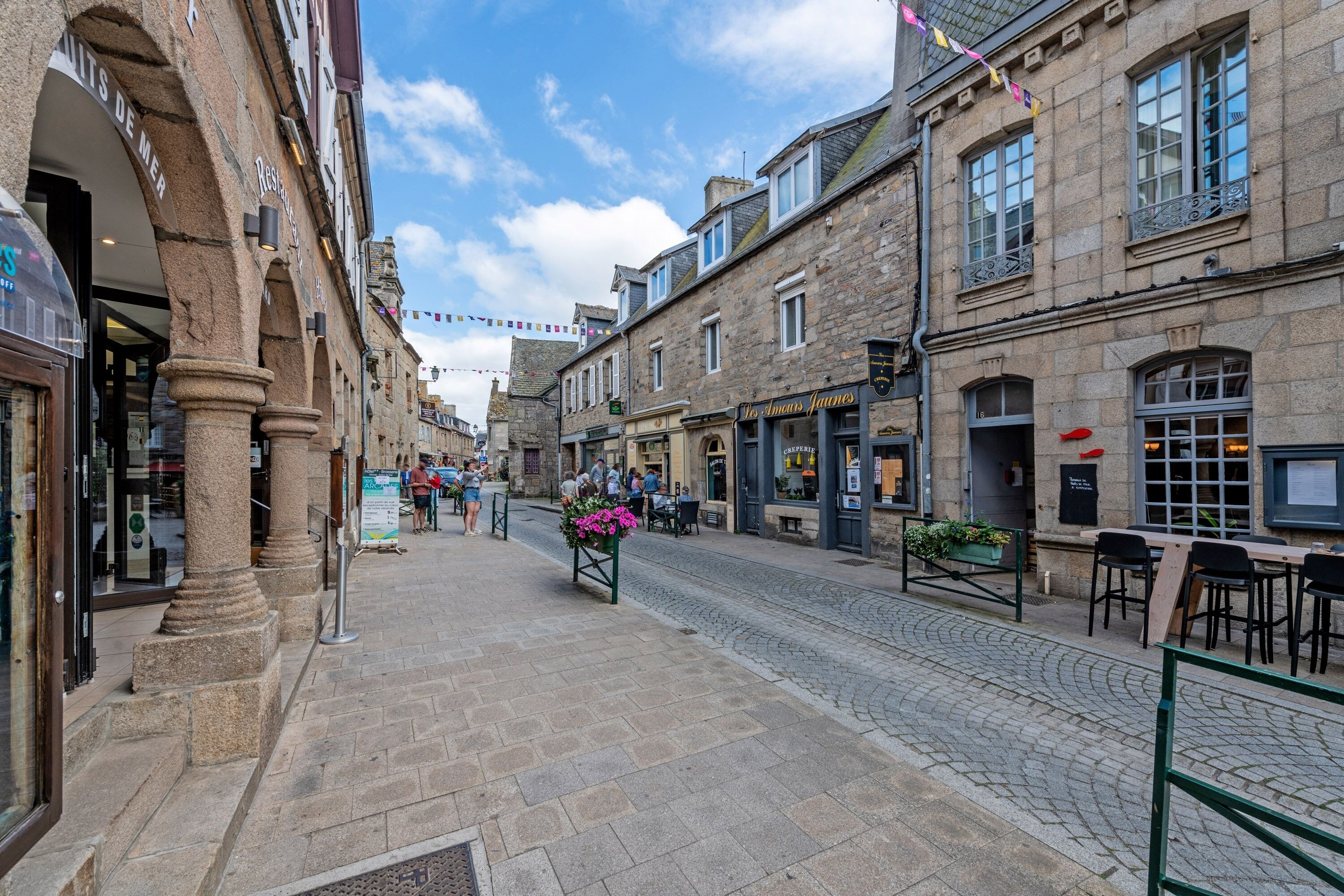 A cobblestone street lined with historic stone buildings, some with signage indicating shops and restaurants.