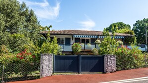 A two-story house with a tiled roof, surrounded by a fence and lush greenery.