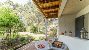 A patio with a round table set for breakfast, surrounded by a garden and trees.