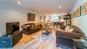 A spacious living room with a large TV, two sofas, a coffee table, and a dining area in the background.