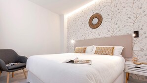 A neatly made bed with a magazine, a grey armchair, and a bedside table with a lamp. - Genteel Home Catedral II (Cadiz)