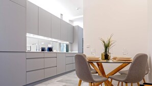 A modern kitchen with grey cabinets, a wooden dining table with grey chairs, and a potted plant on the table. - Genteel Home Catedral II (Cadiz)