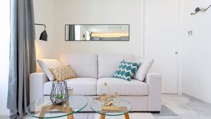 Un salon moderne avec un canapé blanc, une table basse en verre et un coussin à motifs géométriques.