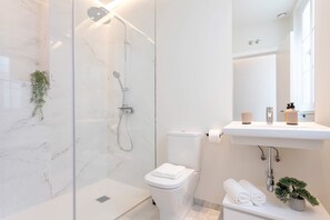 A modern bathroom with a glass-enclosed shower, a toilet, and a sink with a mirror above it. - Genteel Home Catedral IV (Cadiz)