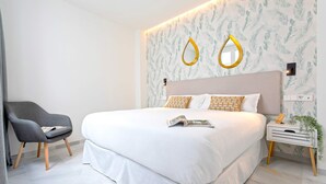 Ein modernes Schlafzimmer mit einem großen Bett, einem grauen Sessel und einem Nachttisch mit einer Pflanze.