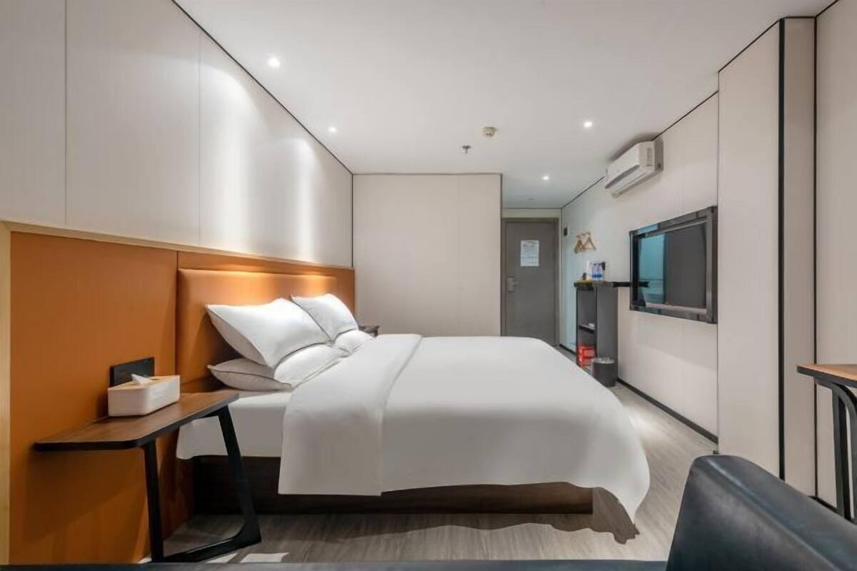 A modern hotel room with a bed, bedside table, TV, and a small desk area.