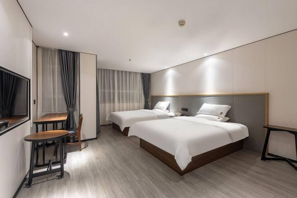 A modern hotel room with two beds, a small table with a chair, and a TV mounted on the wall.