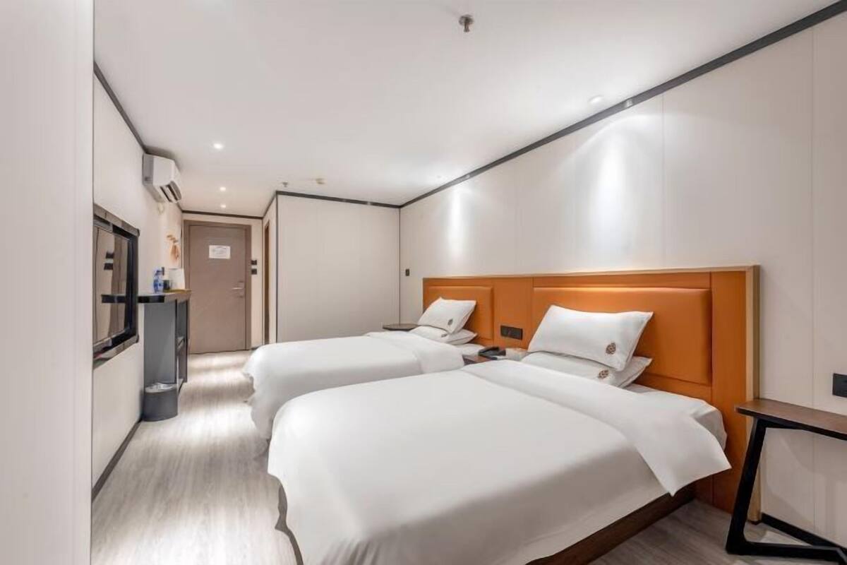 A hotel room with two beds, a desk, a mirror, and a small kitchenette.