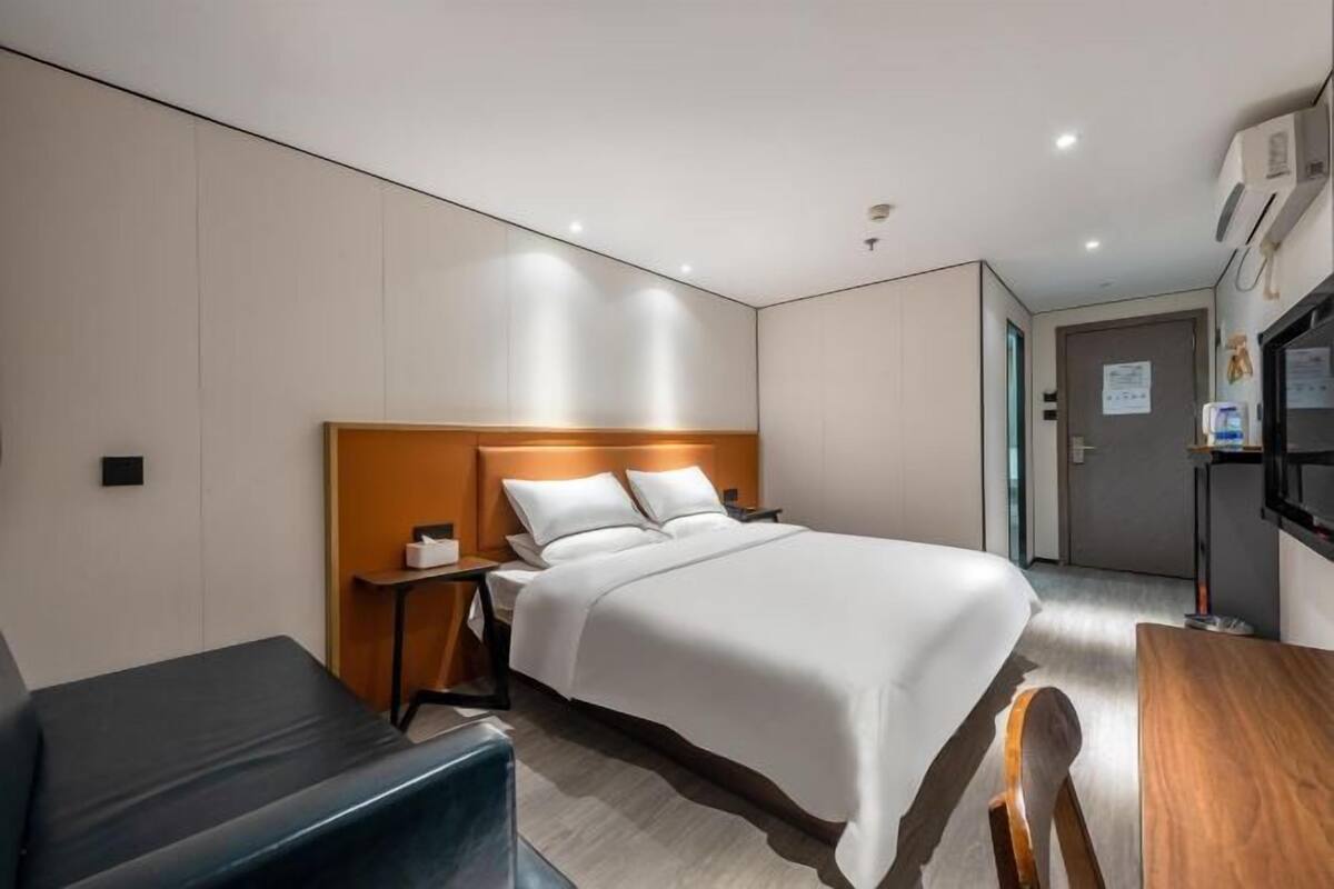 A hotel room with a bed, bedside table, chair, and a desk with a chair.