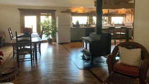 A spacious living area with a wooden floor, a dining table with chairs, a large potted plant, and a modern kitchen with a built-in stove.