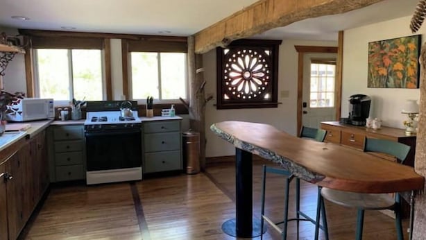 A kitchen with wooden cabinets, a stove, and a bar stool.