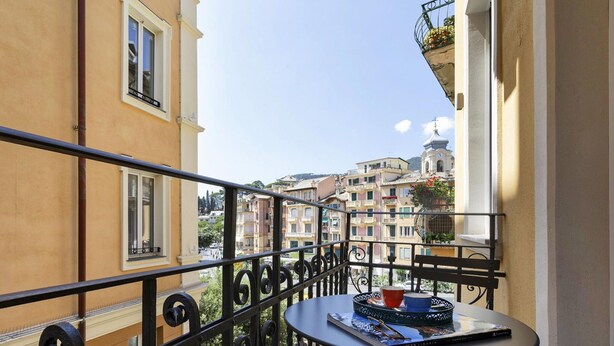 A balcony with a table, a chair, and a view of buildings in the background. - Riviera Flavour Apartments by Wonderful Italy - Valeriana (Santa Margherita Ligure)