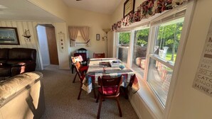 Un comedor acogedor con una mesa dispuesta para cuatro personas, sillas alrededor y vistas a un jardín a través de grandes ventanales.