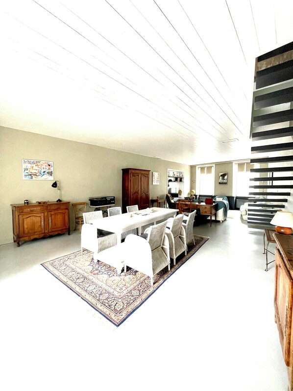 Amplia sala de estar con una gran mesa de comedor, asientos cómodos, una zona de cocina y una escalera.