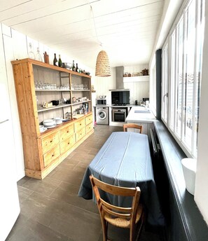 Cocina compacta con comedor, armarios de madera, lavadora y un ventanal amplio.