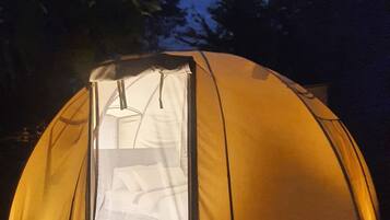 Tenda em forma de cúpula com entrada transparente, sobre um deck de madeira.
