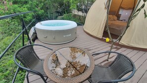 Relax on the deck with a hot tub and a round table amidst lush surroundings.