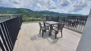 Un balcón con mesa y sillas, vistas a colinas verdes y cielo despejado.