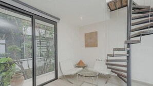 A modern room with a glass door leading to a balcony, a white chair, a small round table, and a wooden spiral staircase. - Royal PH Private Rooftop Deck Pool (Tulum)