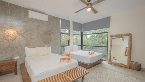 A modern bedroom with two beds, a ceiling fan, large windows, and a wooden bench. - Royal PH Private Rooftop Deck Pool (Tulum)