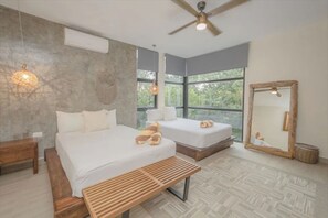 Une chambre moderne avec deux lits, un ventilateur de plafond, de grandes fenêtres et un banc en bois.