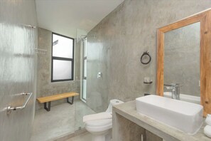 A modern bathroom with a large mirror, a white sink, and a glass-enclosed shower.