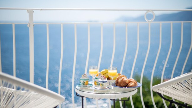 A balcony with a table set for breakfast, including croissants, juice, and a teapot.