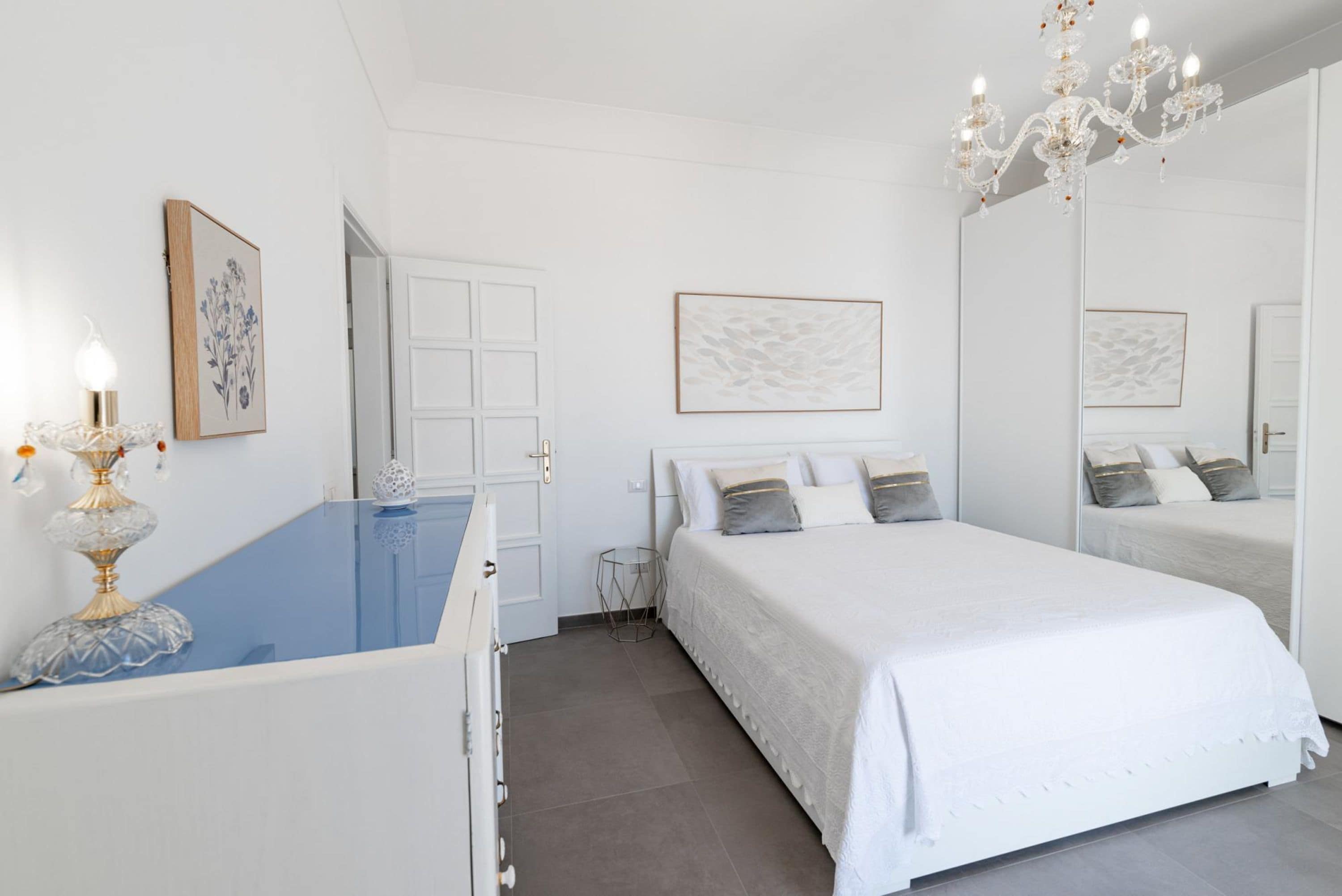 A bedroom with a large bed, a dresser, a mirror, and a chandelier.