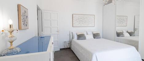 A bedroom with a large bed, a dresser, a mirror, and a chandelier.