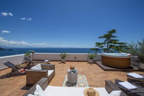 A rooftop terrace with lounge chairs, a hot tub, and potted plants.