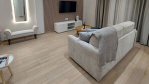 Un salon moderne avec un téléviseur à écran plat fixé au mur, un canapé, une table basse et une table d’appoint sur laquelle se trouve une bouteille.