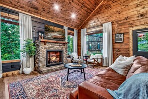 A cozy living room with a stone fireplace, leather sofa, and a large rug.