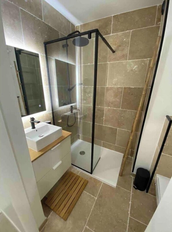 Un baño moderno con cabina de ducha de vidrio, un lavabo blanco y un espejo.