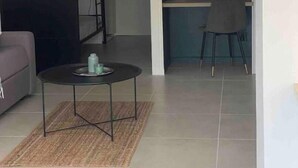 Een moderne woonkamer met een bank, een salontafel en een bureau met een stoel. Er zijn twee ronde ramen in de muur, en een schuifdeur die leidt naar een andere kamer.