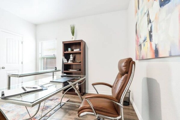 Un espace de bureau moderne avec un bureau en verre, un fauteuil en cuir et une bibliothèque.