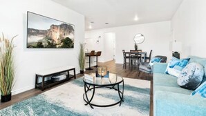 Ein modernes Wohnzimmer mit einem großen Gemälde, einem Glastisch und einem blauen Sofa.