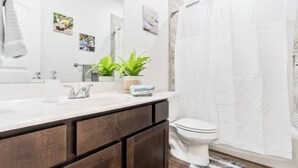 Ein Badezimmer mit einem weißen Waschbecken, dunklen Holzschränken, einer Toilette und einer Duschvorhang.