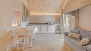A cozy kitchen with white cabinets, a dining table, and a grey sofa.