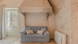 A room with a stone fireplace, a grey sofa with patterned cushions, a white radiator, and a window with curtains.